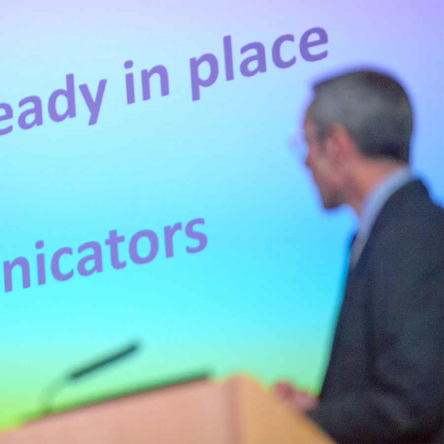 Abstract conference shot with speaker in silhouette against presentation slide
