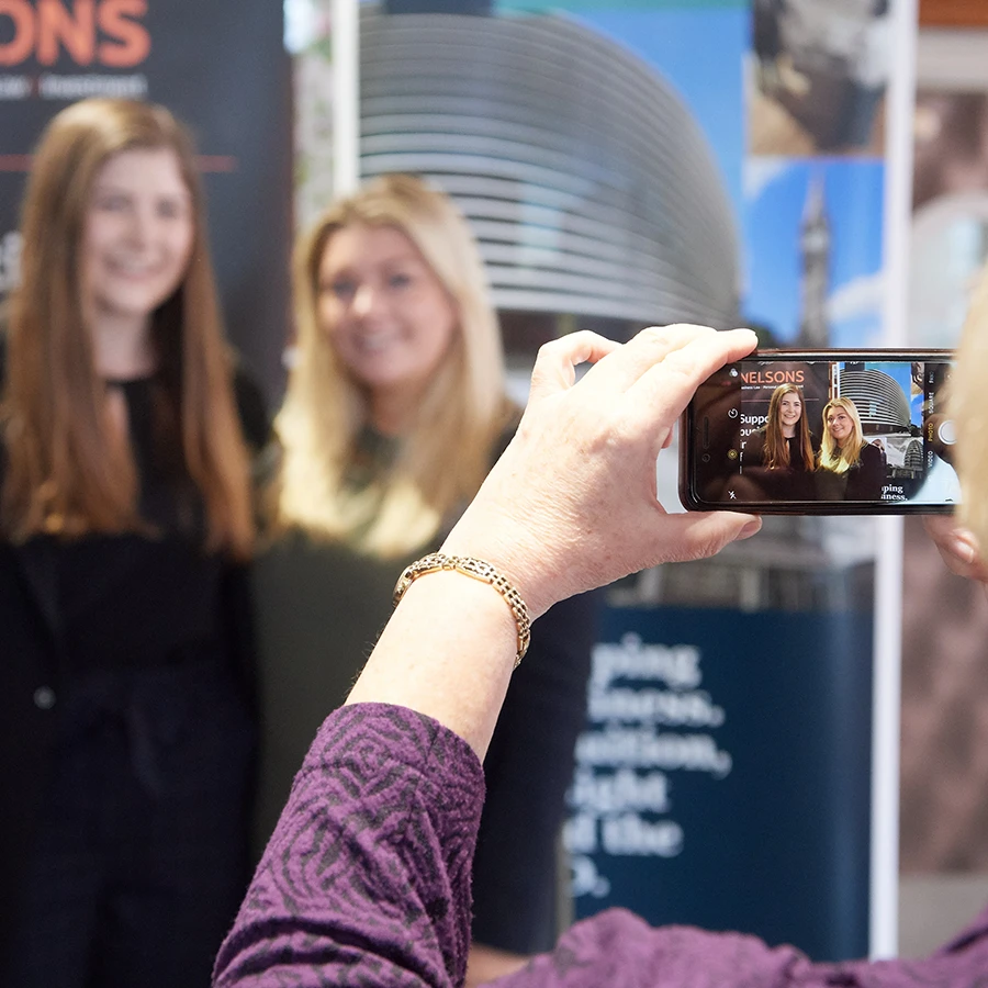 Guest taking a phone photo of attendees in front of a sponsor backdrop at a corporate event
